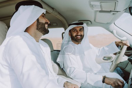 Foto de Dos hombres de Oriente Medio que llevan el tradicional emirati árabe kandura conduciendo un coche 4x4 en el desierto - amigos musulmanes árabes que se reúnen en las dunas de arena en Dubai para una excursión - Imagen libre de derechos