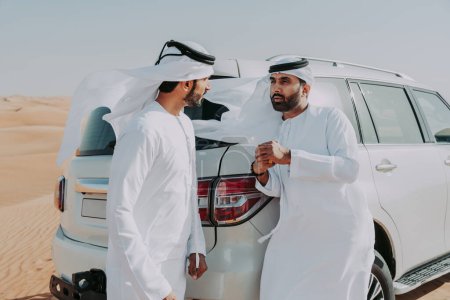 Photo for Two middle-eastern men wearing traditional emirati arab kandura driving a 4x4 car in the desert - Arabian muslim friends meeting at the sand dunes in Dubai for an excursion - Royalty Free Image