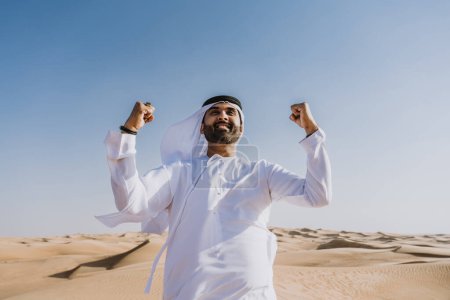 Foto de Hombre guapo y exitoso de Oriente Medio que usa el tradicional emirati árabe kandura en el desierto - árabe musulmán adulto en las dunas de arena en Dubai - Imagen libre de derechos