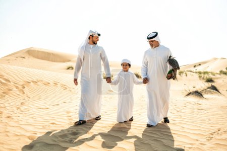 Photo for Three generation family making a safari in the desert of Dubai. Grandfather, son and grandson spending time together in the nature and training their falcon bird. - Royalty Free Image