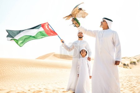 Foto de Familia de tres generaciones haciendo un safari en el desierto de Dubai. Abuelo, hijo y nieto pasando tiempo juntos en la naturaleza y entrenando a su ave halcón. - Imagen libre de derechos