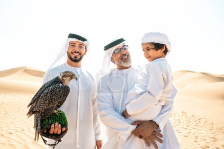 Photo for Three generation family making a safari in the desert of Dubai. Grandfather, son and grandson spending time together in the nature and training their falcon bird. - Royalty Free Image