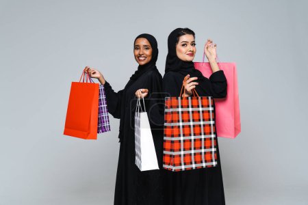 Foto de Hermosas mujeres árabes de Oriente Medio con vestido tradicional abaya y bolsas de compras en el estudio - Retrato femenino árabe musulmán adulto en Dubai, Emiratos Árabes Unidos - Imagen libre de derechos
