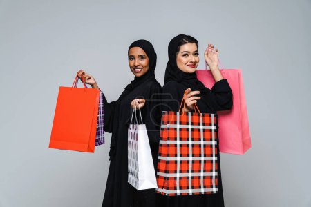 Foto de Hermosas mujeres árabes de Oriente Medio con vestido tradicional abaya y bolsas de compras en el estudio - Retrato femenino árabe musulmán adulto en Dubai, Emiratos Árabes Unidos - Imagen libre de derechos