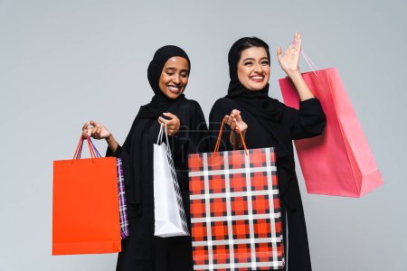 Photo for Beautiful arab middle-eastern women with traditional abaya dress and shopping bags in studio - Arabic muslim adult female portrait in Dubai, United Arab Emirates - Royalty Free Image