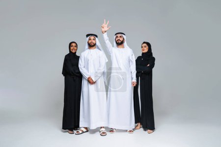Téléchargez les photos : Magnifiques femmes arabes du Moyen-Orient avec une robe traditionnelle abaya et un homme du Moyen-Orient portant une kandora en studio - Groupe d'adultes arabes musulmans portrait à Dubaï, Émirats arabes unis - en image libre de droit