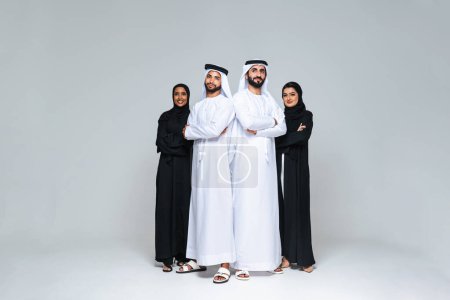 Photo for Beautiful arab middle-eastern women with traditional abaya dress and middle easter man wearing kandora in studio - Group of arabic muslim adults portrait in Dubai, United Arab Emirates - Royalty Free Image