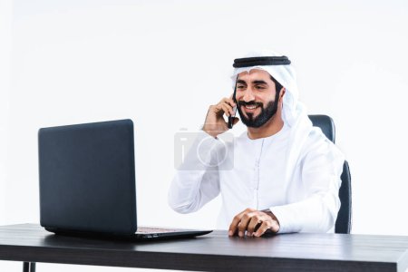Photo for Emirate middle-eastern businessman wearing kandora working in the office, Dubai - Handsome corporate business man sitting at computer desk and remote working with laptop - Royalty Free Image