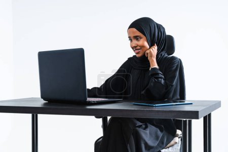 Foto de Hermosa mujer de negocios corporativa árabe de Oriente Medio con vestido tradicional abaya que trabaja en la oficina- retrato femenino musulmán árabe adulto en el escritorio de la computadora en Dubai, Emiratos Árabes Unidos - Imagen libre de derechos