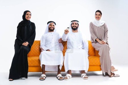 Téléchargez les photos : Beau arabe Moyen-Orient heureux groupe d'amis portant traditionnel abaya et kandora collage à la maison - Arabe musulmans adultes assis sur le canapé et s'amuser à Dubaï, Émirats arabes unis - en image libre de droit