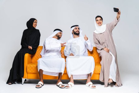 Photo for Beautiful arab middle-eastern happy group of friends wearing traditional abaya and kandora bonding at home - Arabic muslim adult people sitting on the sofa and having fun in Dubai, United Arab Emirates - Royalty Free Image