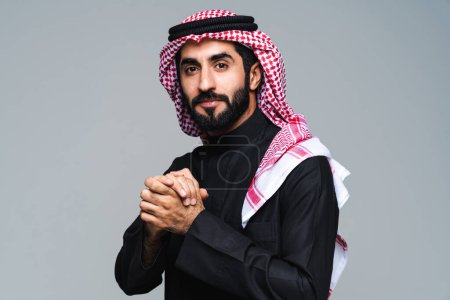 Téléchargez les photos : Bel homme arabe saoudien du Moyen-Orient avec des vêtements traditionnels saoudiens en studio - homme d'affaires arabe musulman adulte portant un portrait de thwab isolé sur fond gris - en image libre de droit