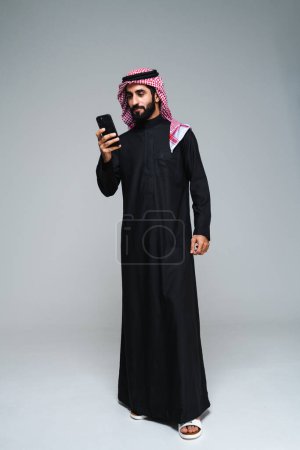 Photo for Handsome arab middle-eastern saudi arabian man with traditional saudi clothing in studio - Arabic muslim adult male businessman wearing thwab portrait isolated on gray background - Royalty Free Image