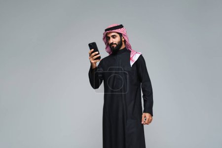 Photo for Handsome arab middle-eastern saudi arabian man with traditional saudi clothing in studio - Arabic muslim adult male businessman wearing thwab portrait isolated on gray background - Royalty Free Image