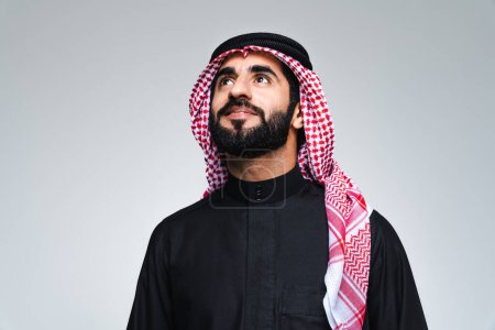 Foto de Hombre guapo árabe de Oriente Medio con ropa tradicional saudí en el estudio - Hombre árabe musulmán adulto hombre de negocios con retrato thwab aislado sobre fondo gris - Imagen libre de derechos