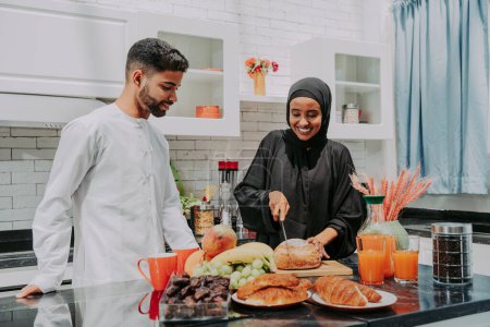 Téléchargez les photos : Heureux couple moyen-oriental vêtu de vêtements arabes traditionnels à la maison - mari et femme arabes mariés se lient dans l'appartement, concepts sur la relation, la vie domestique et le mode de vie emirati - en image libre de droit