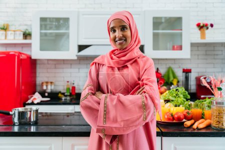 Téléchargez les photos : Joyeux Moyen-Orient femme portant abaya à la maison - Magnifique portrait de femme musulmane adulte dans l'appartement, concepts sur la vie domestique et le mode de vie islamique - en image libre de droit