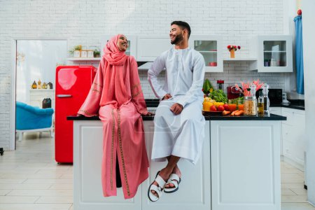 Téléchargez les photos : Heureux couple moyen-oriental vêtu de vêtements arabes traditionnels à la maison - mari et femme arabes mariés se lient dans l'appartement, concepts sur la relation, la vie domestique et le mode de vie emirati - en image libre de droit