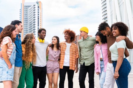 Téléchargez les photos : Heureux groupe multiethnique ludique de jeunes amis qui se lient en plein air étudiants multiraciaux milléniaux se réunissant dans la ville, concepts de la jeunesse, mode de vie des gens, la diversité, l'adolescence et la vie urbaine - en image libre de droit