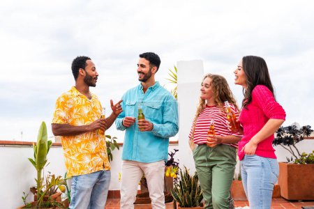 Téléchargez les photos : Groupe multiethnique de jeunes amis heureux dîner barbecue partie sur le toit à la maison - Multiracial jeunes adultes joyeux s'amuser et coller sur un balcon terrasse avec vue sur la ville, manger et boire. - en image libre de droit