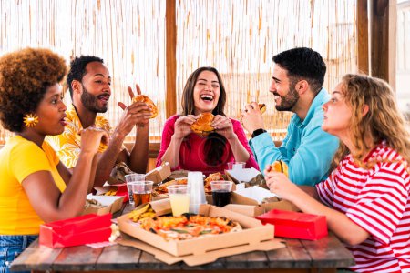 Téléchargez les photos : Groupe multiethnique de jeunes amis heureux dîner barbecue partie sur le toit à la maison - Multiracial jeunes adultes joyeux s'amuser et coller sur un balcon terrasse avec vue sur la ville, manger et boire. - en image libre de droit
