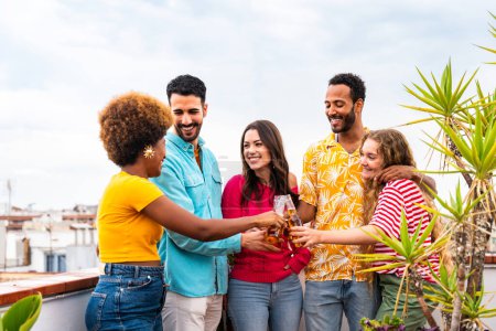 Photo for Multiethnic group of happy young friends having dinner barbecue party on rooftop at home - Multiracial cheerful young adult people having fun and bonding on a terrace balcony with city view, eating and drinking. - Royalty Free Image