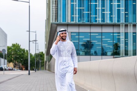 Photo for Arab middle-eastern man wearing emirati kandora traditional clothing in the city - Arabian muslim businessman strolling in urban business centre. - Royalty Free Image