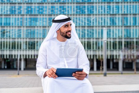 Photo for Arab middle-eastern man wearing emirati kandora traditional clothing in the city - Arabian muslim businessman strolling in urban business centre. - Royalty Free Image