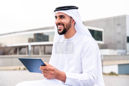 Téléchargez les photos : Homme arabe du Moyen-Orient portant des vêtements traditionnels emirati kandora dans la ville - Homme d'affaires musulman arabe se promenant dans le centre d'affaires urbain. - en image libre de droit