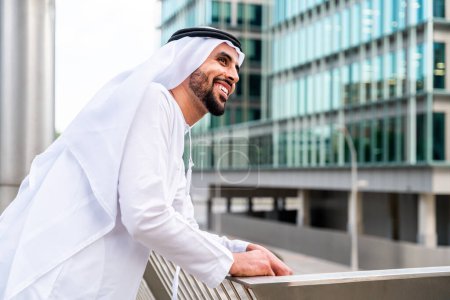 Téléchargez les photos : Homme arabe du Moyen-Orient portant des vêtements traditionnels emirati kandora dans la ville - Homme d'affaires musulman arabe se promenant dans le centre d'affaires urbain. - en image libre de droit