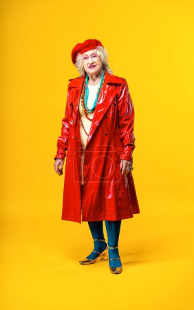 Foto de Hermosa anciana mayor con ropa de fiesta de lujo actuando sobre un fondo de color en el estudio - Imagen conceptual sobre la tercera edad y la antigüedad, las personas mayores se sienten jóvenes dentro. - Imagen libre de derechos