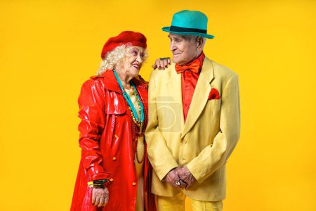 Téléchargez les photos : Beau vieux couple de personnes âgées portant des vêtements de fête fantaisie agissant en studio sur un fond coloré. Image conceptuelle sur le troisième âge et l'ancienneté, les personnes âgées se sentent jeunes à l'intérieur. - en image libre de droit