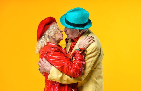 Téléchargez les photos : Beau vieux couple de personnes âgées portant des vêtements de fête fantaisie agissant en studio sur un fond coloré. Image conceptuelle sur le troisième âge et l'ancienneté, les personnes âgées se sentent jeunes à l'intérieur. - en image libre de droit