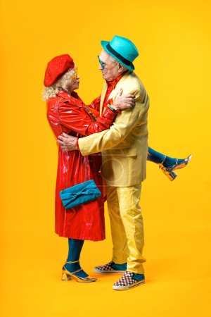 Foto de Hermosa pareja de ancianos vistiendo ropa de fiesta de lujo actuando en el estudio sobre un fondo de color. Imagen conceptual sobre la tercera edad y la antigüedad, los ancianos sintiéndose jóvenes por dentro. - Imagen libre de derechos