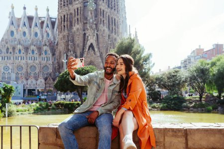 Photo for Multiracial beautiful happy couple of lovers dating at Sagrada Familia, Barcelona - Multiethnic tourists travelling in Europe and visiting a city in Spain, concepts about tourism and people lifestyle - Royalty Free Image