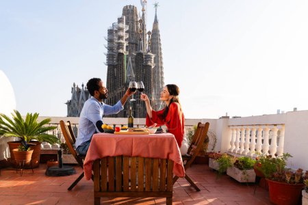 Téléchargez les photos : Multiracial beau couple heureux d'amoureux datant sur le balcon sur le toit à la Sagrada Familia, Barcelone - Les gens multiethniques ayant dîner apéritif romantique sur une terrasse avec vue sur la ville, concepts sur le tourisme et le mode de vie des gens - en image libre de droit