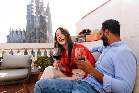 Photo for Multiracial beautiful happy couple of lovers dating on rooftop balcony at Sagrada Familia, Barcelona - Multiethnic people having romantic aperitif on a terrace with city view , concepts about tourism and people lifestyle - Royalty Free Image