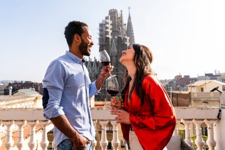 Foto de Multiracial hermosa pareja feliz de amantes citas en el balcón de la azotea en Sagrada Familia, Barcelona - Personas multiétnicas que tienen aperitivo romántico en una terraza con vista a la ciudad, conceptos sobre el turismo y el estilo de vida de las personas - Imagen libre de derechos