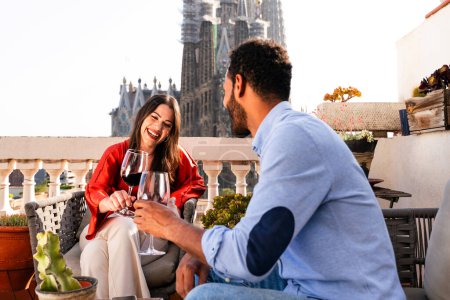 Photo for Multiracial beautiful happy couple of lovers dating on rooftop balcony at Sagrada Familia, Barcelona - Multiethnic people having romantic aperitif on a terrace with city view , concepts about tourism and people lifestyle - Royalty Free Image