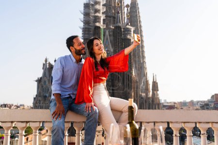 Téléchargez les photos : Multiracial beau couple heureux d'amoureux datant sur le balcon sur le toit à la Sagrada Familia, Barcelone - Les gens multiethniques ayant une réunion romantique sur une terrasse avec vue sur la ville, concepts sur le tourisme et le mode de vie des gens - en image libre de droit