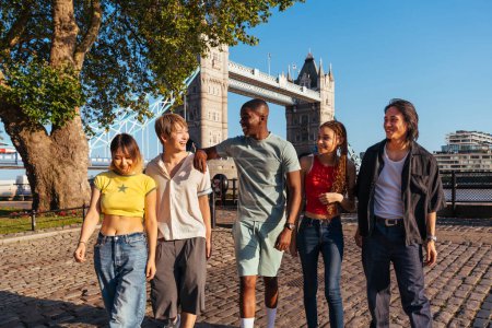 Foto de Grupo multirracial de jóvenes amigos felices que se unen en la ciudad de Londres - Estudiantes adolescentes multiétnicos que se reúnen y se divierten en el área de Tower Bridge, Reino Unido - Conceptos sobre estilo de vida juvenil, viajes y turismo - Imagen libre de derechos
