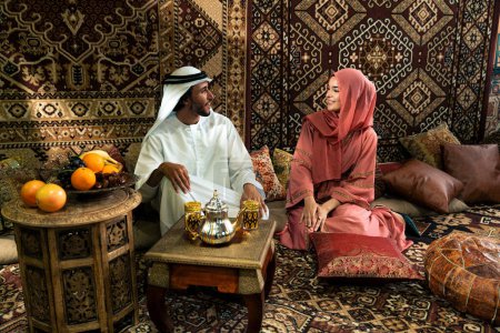 Foto de Parejas jóvenes de Emirati pasan tiempo en un café tradicional árabe. Hombre y mujer usando kandura y abaya de Dubai conversando juntos. - Imagen libre de derechos