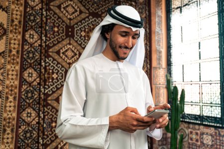 Téléchargez les photos : Homme d'emirati en tenue de kandura passant du temps dans une maison traditionnelle arabe à Dubaï - en image libre de droit