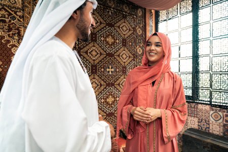 Téléchargez les photos : Un jeune couple émirien passe du temps dans un café arabe traditionnel. Homme et femme portant kandura et abaya de Dubaï conversant ensemble. - en image libre de droit