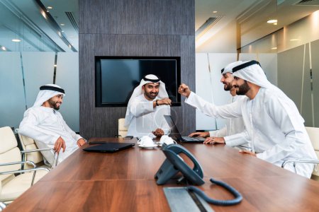 Gruppe arabischer Geschäftsleute trifft sich im Büro - Geschäftsleute aus dem Nahen Osten tragen emiratische Kandora bei der Arbeit in einem Besprechungsraum, Dubai