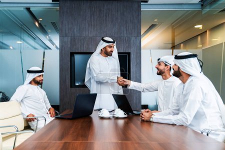 Gruppe arabischer Geschäftsleute trifft sich im Büro - Geschäftsleute aus dem Nahen Osten tragen emiratische Kandora bei der Arbeit in einem Besprechungsraum, Dubai