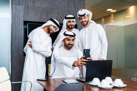 Téléchargez les photos : Groupe d'hommes d'affaires arabes d'entreprise réunis dans le bureau - Des hommes d'affaires du Moyen-Orient portant des emirati kandora travaillant dans une salle de réunion, Dubaï - en image libre de droit