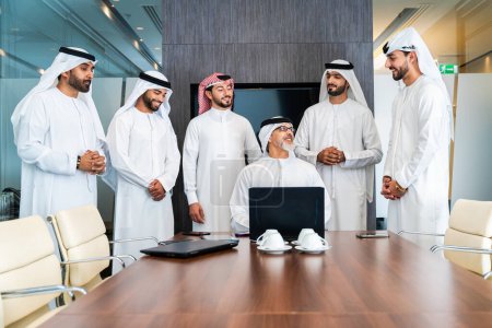 Foto de Grupo de empresarios árabes corporativos reunidos en la oficina - Empresarios de Oriente Medio que usan emirati kandora trabajando en una sala de reuniones, Dubai - Imagen libre de derechos