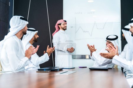 Photo for Group of corporate arab businessmen meeting in the office - Middle-eastern businesspeople wearing emirati kandora working in a meeting room, Dubai - Royalty Free Image