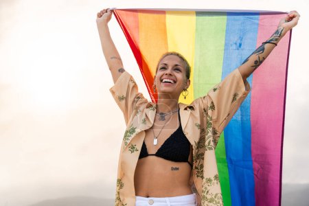 Téléchargez les photos : Belle lesbienne tenant le drapeau LGBT à la plage, concepts sur la communauté LGBTQ, diversité, amour et mode de vie - en image libre de droit